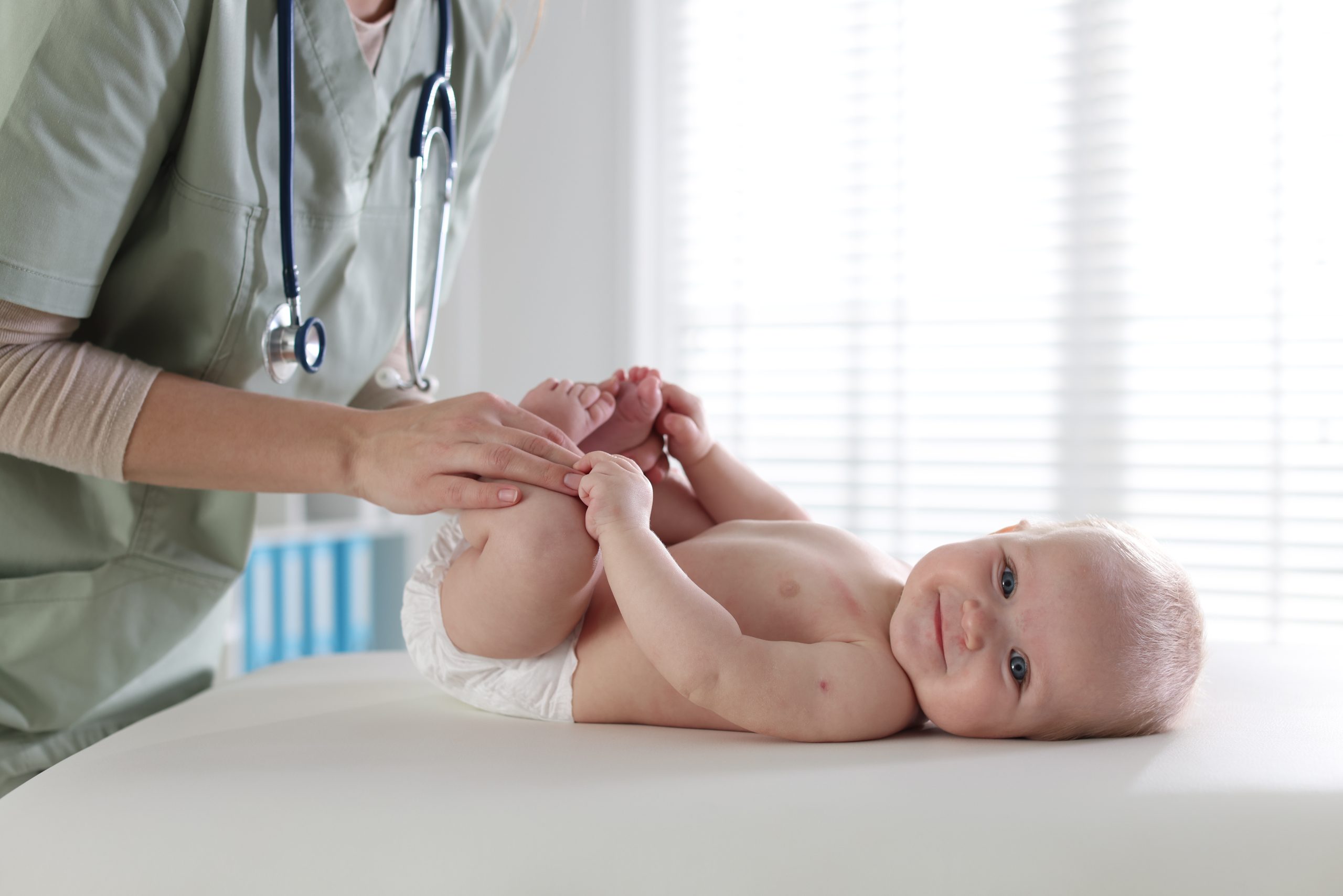 Pediatrician gently examining a smiling newborn baby on an exam table in a bright clinic room